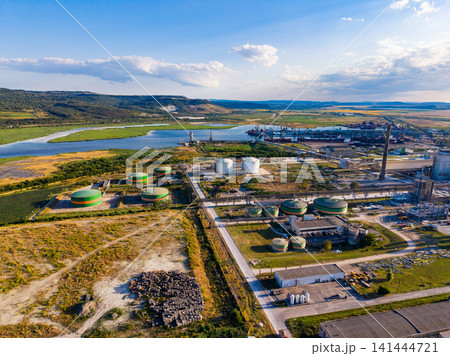Industrial area near a river with storage tanks, pipelines, and factories under a clear sky in daytime 141444721