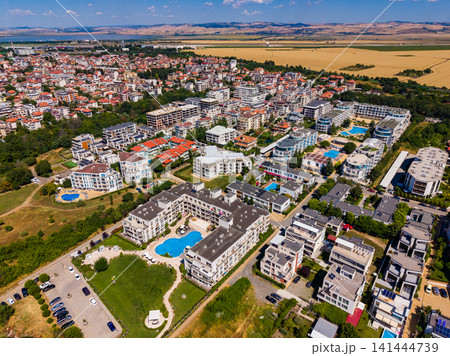 View of a residential area with buildings, swimming pools, and green spaces in a town surrounded by fields on a clear day View of a residential area with buildings, swimming pools, and green spaces in a town surrounded by fields on a clear day 141444739