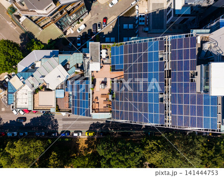 Solar panels cover rooftops of buildings in an urban area with trees and parked cars on a sunny day 141444753