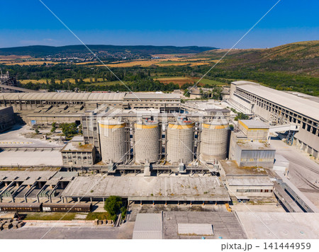 Industrial facility located in a rural area with large storage silos and machinery visible against a clear blue sky Industrial facility located in a rural area with large storage silos and machinery visible against a clear blue sky 141444959