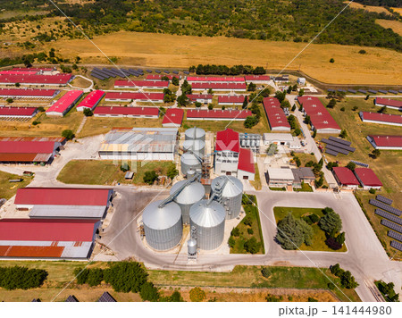 Farm complex with grain silos and storage buildings seen from above in rural area during daytime Farm complex with grain silos and storage buildings seen from above in rural area during daytime 141444980