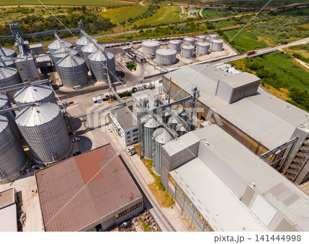 View of a large industrial facility with silos and storage tanks during midday 141444998