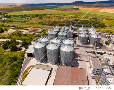 View of grain storage facility in rural area during daytime with fields and hills in background 141444999