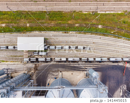 Freight trains lined up at a rail yard with storage silos and tracks visible from above Freight trains lined up at a rail yard with storage silos and tracks visible from above 141445015