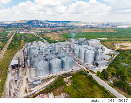 Grain storage facility located on the outskirts of a city with trains and vehicles nearby during daylight Grain storage facility located on the outskirts of a city with trains and vehicles nearby during daylight 141445017