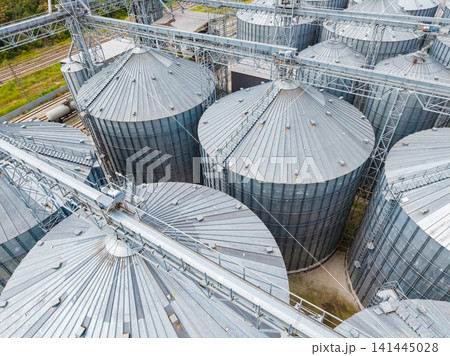 Large metal storage silos are arranged in rows at a grain facility during daylight hours in a rural area 141445028