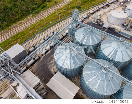 Grain storage facility near railway tracks with multiple silos and loading equipment during daytime 141445041