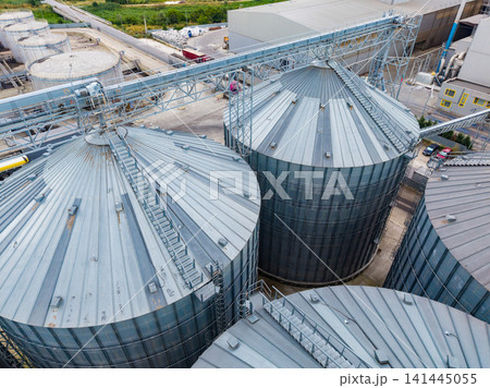 Large metal storage tanks are seen from above at an industrial site near fields and buildings during the day Large metal storage tanks are seen from above at an industrial site near fields and buildings during the day 141445055