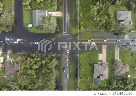 Hurricane flooded street with moving cars and surrounded with water houses in Florida residential area. Consequences of natural disaster Hurricane flooded street with moving cars and surrounded with water houses in Florida residential area. Consequences of natural disaster 141445110