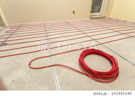 Heating red electrical cable wire roll on cement floor copy space background. Renovation and construction, comfortable warm home concept. Heating red electrical cable wire roll on cement floor copy space background. Renovation and construction, comfortable warm home concept. 141445140