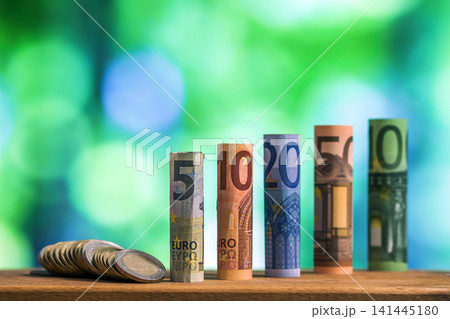 Five, ten, twenty, fifty and one hundred euro rolled bills banknotes, with euro coins on green blurred bokeh background. Five, ten, twenty, fifty and one hundred euro rolled bills banknotes, with euro coins on green blurred bokeh background. 141445180