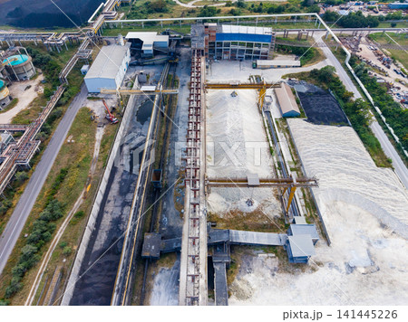 Industrial site with large structures, conveyor systems, and piles of materials captured from above on a clear day Industrial site with large structures, conveyor systems, and piles of materials captured from above on a clear day 141445226
