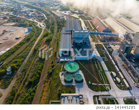 Factory site with large buildings, industrial equipment, and green tanks showing process and activity during daytime hours Factory site with large buildings, industrial equipment, and green tanks showing process and activity during daytime hours 141445285