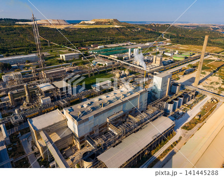 Industrial complex near a mining site shows various structures and pipelines during daytime with green landscape and a distant hill Industrial complex near a mining site shows various structures and pipelines during daytime with green landscape and a distant hill 141445288