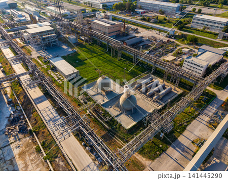 Industrial site with pipes and storage tanks located near a manufacturing area during daylight hours Industrial site with pipes and storage tanks located near a manufacturing area during daylight hours 141445290