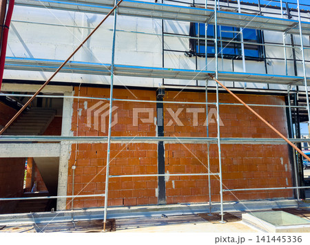 Construction work is in progress on a building with a focus on scaffolding and brick wall at a site during a sunny day Construction work is in progress on a building with a focus on scaffolding and brick wall at a site during a sunny day 141445336