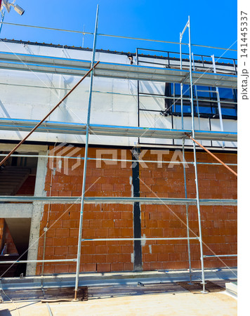 Construction workers build a wall using bricks and scaffolding at a site during a sunny day in the city Construction workers build a wall using bricks and scaffolding at a site during a sunny day in the city 141445337