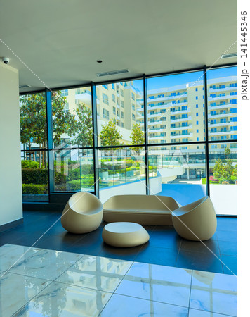 Modern seating area with large windows showing outdoor pool and buildings during daytime in a residential complex setting Modern seating area with large windows showing outdoor pool and buildings during daytime in a residential complex setting 141445346