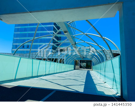 Modern walkway covered with glass and metal structure in a city setting under bright blue sky 141445350