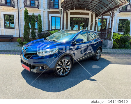 Car parked outside a large building with a roof and trees in the background during a sunny day Car parked outside a large building with a roof and trees in the background during a sunny day 141445430