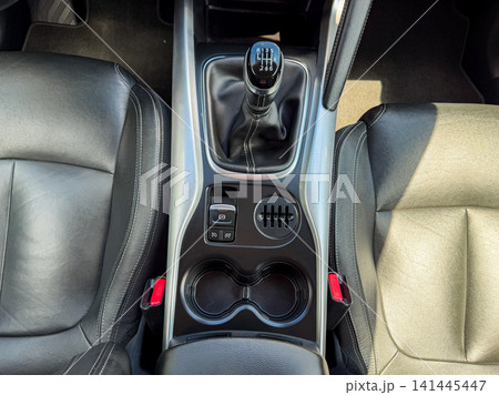 View of a car center console with manual gear shift and cup holders, taken inside a vehicle during daytime View of a car center console with manual gear shift and cup holders, taken inside a vehicle during daytime 141445447