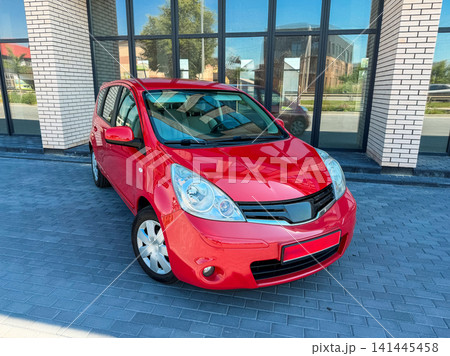 Bright red car parked outside a modern building in a city during the day with clear skies and no people around Bright red car parked outside a modern building in a city during the day with clear skies and no people around 141445458
