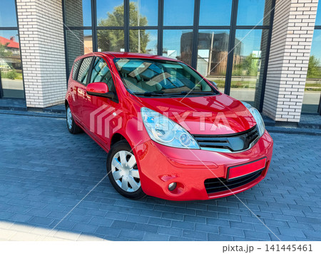 Bright red car parked near a modern building with large glass windows on a sunny day 141445461