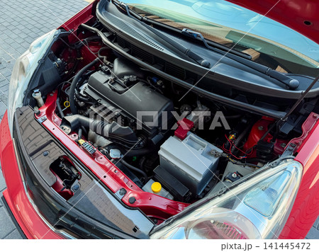 Engine view of a red car with open hood showing various parts and components in a parking lot setting 141445472