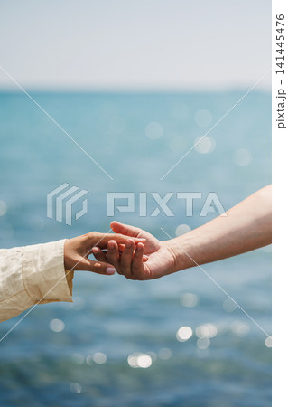 Two hands reach out to each other against the backdrop of the ocean on a sunny day near the shore Two hands reach out to each other against the backdrop of the ocean on a sunny day near the shore 141445476