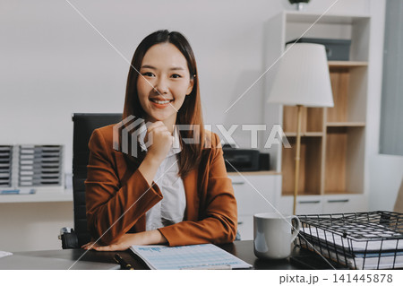 Young Asian professional business woman calculating finances and analyzing data charts on computer, smiling while working on accounting project in a modern office, planning budget Young Asian professional business woman calculating finances and analyzing data charts on computer, smiling while working on accounting project in a modern office, planning budget 141445878