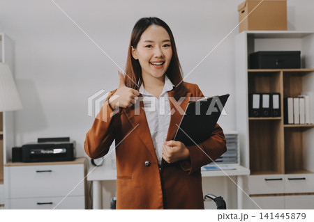 Young Asian professional business woman calculating finances and analyzing data charts on computer, smiling while working on accounting project in a modern office, planning budget Young Asian professional business woman calculating finances and analyzing data charts on computer, smiling while working on accounting project in a modern office, planning budget 141445879