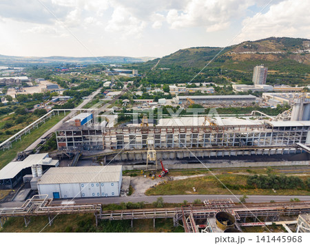 Industrial site with large buildings and machinery near a body of water in a rural area on a cloudy day 141445968