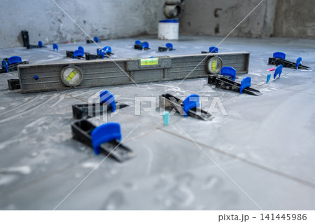 Tiler installing new ceramic floor tiles with a tile leveling system, ensuring even surfaces for house renovation work on a construction site 141445986