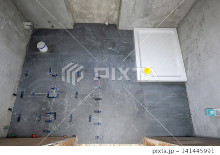 Bathroom floor being tiled with dark grey ceramic tiles and leveling system, installing a new white shower tray as part of a house renovation project Bathroom floor being tiled with dark grey ceramic tiles and leveling system, installing a new white shower tray as part of a house renovation project 141445991