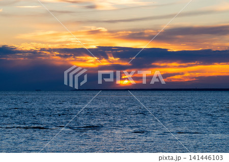 Sun sets behind dark clouds over deep blue sea. Beautiful orange sky with golden rays reflecting on water. Concept of hope and tranquility. Natural sunset background. Sun sets behind dark clouds over deep blue sea. Beautiful orange sky with golden rays reflecting on water. Concept of hope and tranquility. Natural sunset background. 141446103