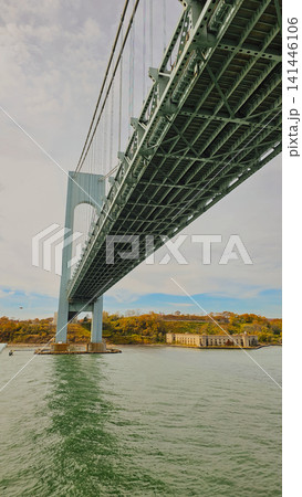 Low angle view of Verrazzano Narrows suspension bridge structure spanning over water passage as vessel passes underneath in New York for maritime transport concept Low angle view of Verrazzano Narrows suspension bridge structure spanning over water passage as vessel passes underneath in New York for maritime transport concept 141446106