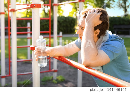 Tired man resting after an outdoor gym workout. Exhausted athlete with water bottle and towel taking a break from fitness training on a sunny summer day. Tired man resting after an outdoor gym workout. Exhausted athlete with water bottle and towel taking a break from fitness training on a sunny summer day. 141446145