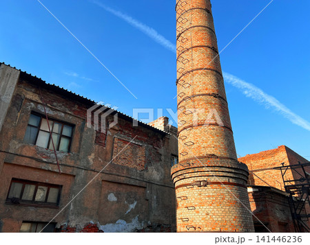 Abandoned brick industrial building with tall chimney and broken windows against clear blue sky Abandoned brick industrial building with tall chimney and broken windows against clear blue sky 141446236