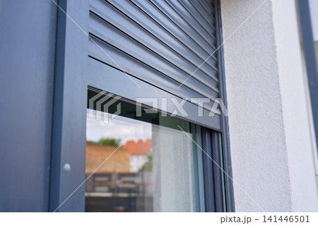 Exterior roller shutter covers the upper part of house window beside white facade Exterior roller shutter covers the upper part of house window beside white facade 141446501