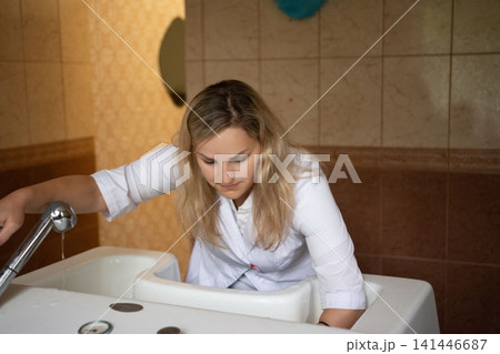 A professional fills a bathtub with water. She is wearing a white shirt and is working in a bathroom that is clean. 141446687