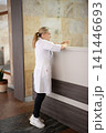 Healthcare worker in uniform checking her phone at a reception desk, standing against stone wall, wearing black leggings and white shoes. 141446693