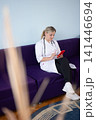 Doctor on a break, sitting on a purple couch, engrossed in her mobile phone. The scene evokes a moment of personal time in a professional setting. 141446694