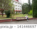 Medical professional takes a call while seated on a park bench outside a building with green trees surrounding the scene. Relaxing break. 141446697