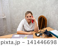 A healthcare provider is multitasking, conversing on a mobile phone while seemingly reviewing data on a computer at a light-colored desk. 141446698
