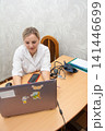 Healthcare professional working on laptop. Telemedicine consult or administrative work in a clinical setting. Woman in white coat with stethoscope. 141446699