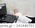 Medical professional lies next to an ultrasound machine. She is relaxing while waiting for her patient. Medical scan equipment is present. 141446701