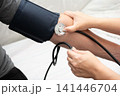 Healthcare provider using stethoscope and blood pressure cuff on a patient's arm to measure blood pressure in medical setting. 141446704