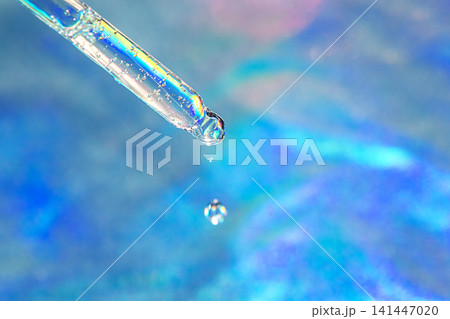 Macro shot of a glass dropper releasing a water droplet over an iridescent blue background for skincare Macro shot of a glass dropper releasing a water droplet over an iridescent blue background for skincare 141447020