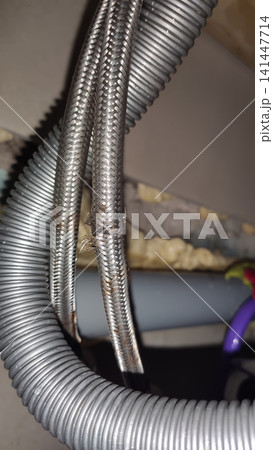 Damaged flexible hose with a metal braided sheath showing visible tears, corrosion, and signs of wear. Damaged flexible hose with a metal braided sheath showing visible tears, corrosion, and signs of wear. 141447714