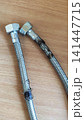 Damaged flexible hose with a metal braided sheath showing visible tears, corrosion, and signs of wear. 141447715